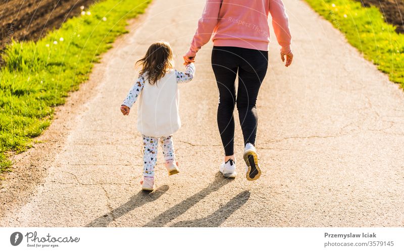 Mother and child walking on countryside road between agricultural fields towards forest in Austrian vilage durring sunset. daughter fit healthy people caucasian