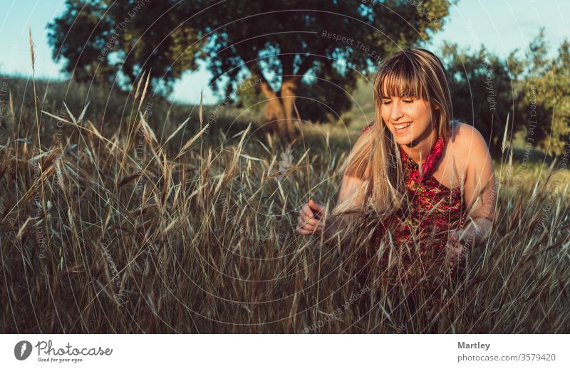 Beautiful young blonde model smiling in a field at sunset wearing dress. Happy free woman in nature. Cozy photography. back girl happy smile sunshine around