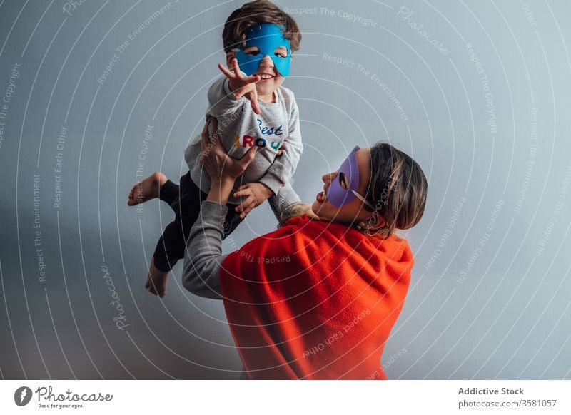 Smiling mother playing with son at home superhero toss mask game having fun boy together pretend creative playful cheerful little weekend kid child happy