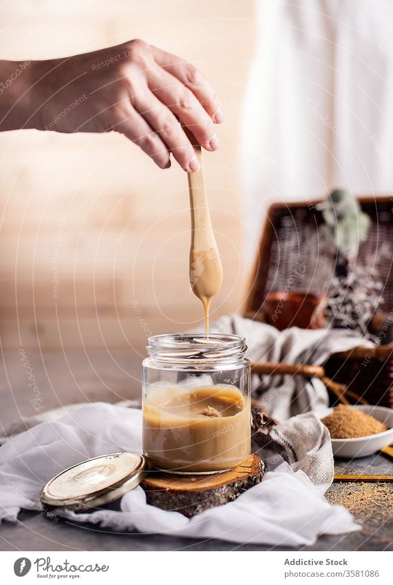 Crop woman preparing caramel at table in light modern kitchen jar teaspoon hand sugar fabric homemade dessert treat ingredient tasty gastronomy female sweet