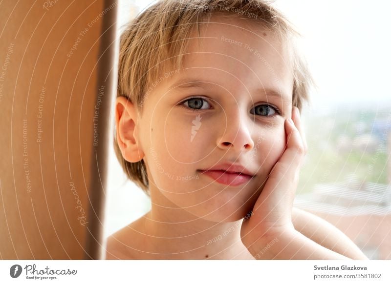 Portrait young caucasian cute boy with blond hair inside the house near the window. Calm emotion portrait child face kid white person childhood male blonde