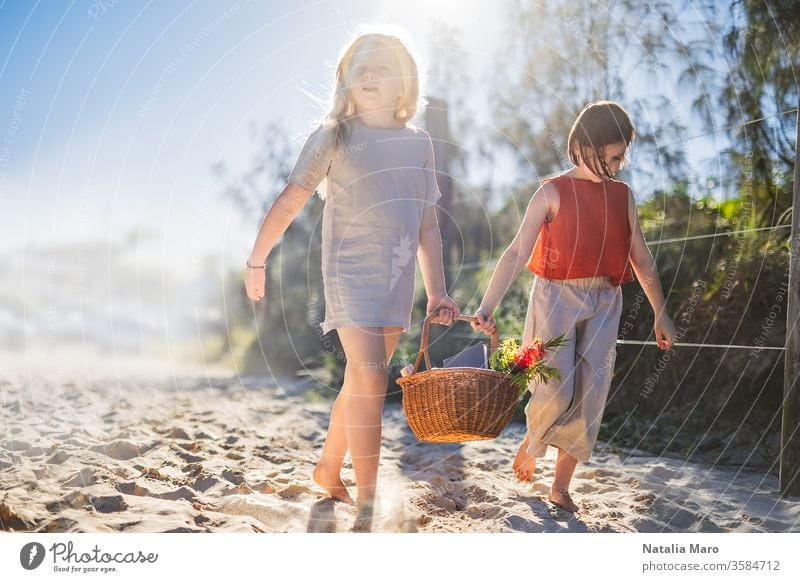 Little girls walking barefoot on the sand and caring a picnic basket together. Summer leisure, love and friendship. nature park child activity summer recreation