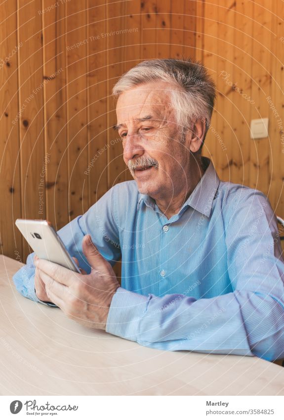 Happy gray-haired older man using a smartphone, making a video call to his grandchildren or family at home during the coronavirus. Watching funny videos on social networks.