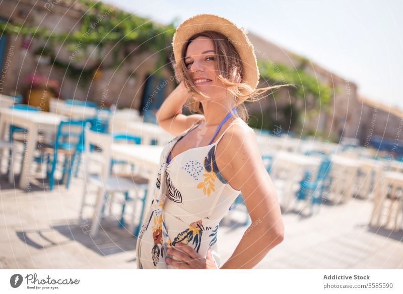 Stylish young woman in summer dress on cafe terrace in old town straw hat street exterior style building sandal entrance plant aged allure facade outfit