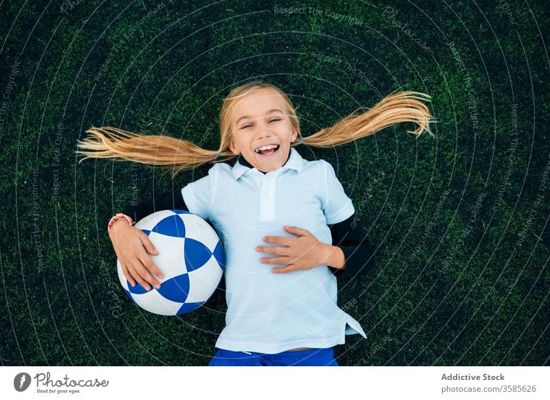 Cheerful girl player with soccer ball relaxing on lawn laugh field football ponytail stadium child kid preteen happy playful optimist uniform equipment sporty