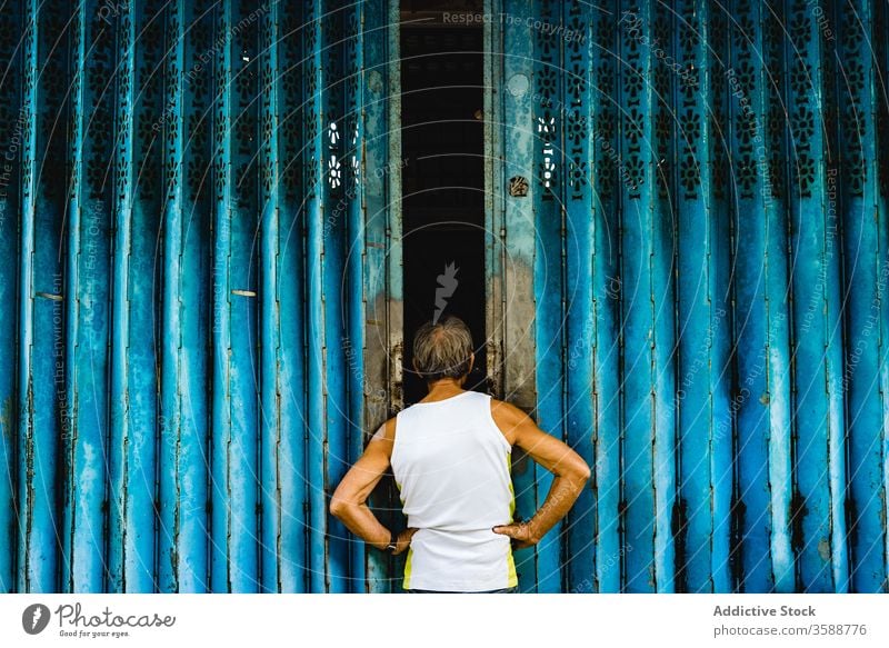 Aged local man looking inside of ornamental doors district metal exterior city doorway blue building old street culture tradition industrial hong kong china