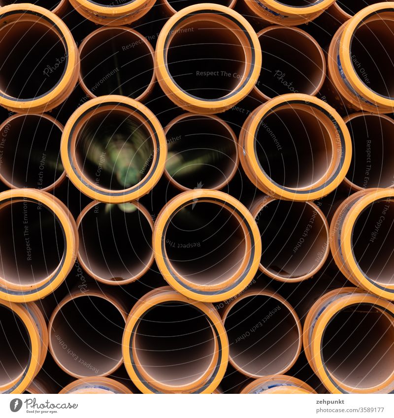 Many orange tubes seen from the front side. In three of them the green of the background shimmers out. pipes Orange Construction site Stack Black circles