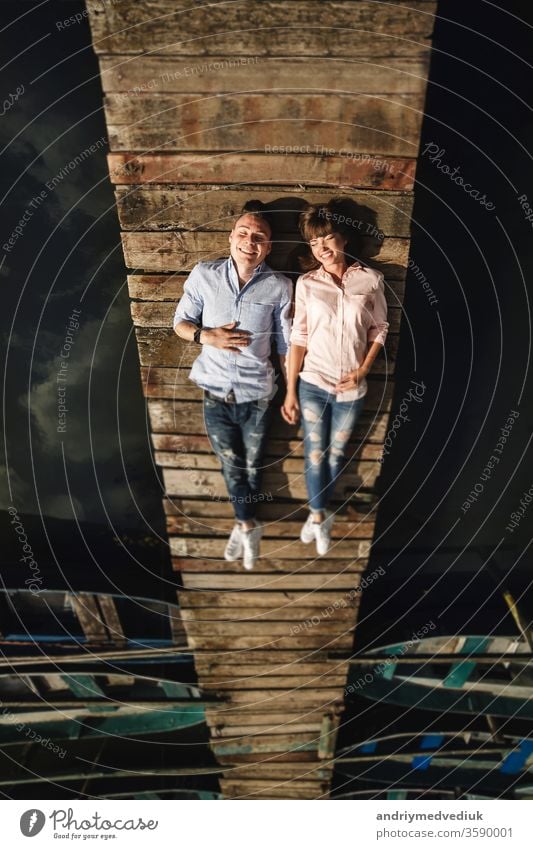 Perfect date. Beautiful young couple and lying smiling on the pier. Happy young man and woman lying laughing on the wooden pier by the water loosen up luck Love