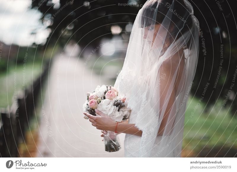 Beautiful young bride in a white luxury dress and in a bridal veil with a bouquet of flowers posing outdoor. wedding portrait. copy space beauty beautiful