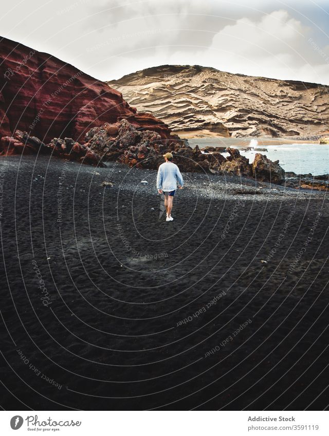 Traveling man walking along black beach during vacation sand traveler tourist mountain summer colorful male nature outfit cloudy landscape scenic trip tourism