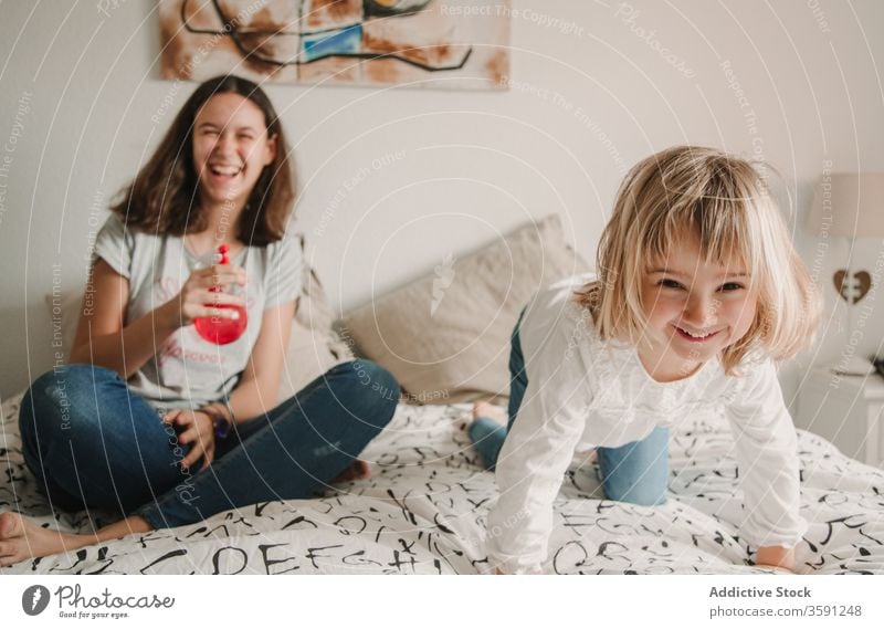 Playful sisters having fun with pulverizer at home play sprayer water weekend together cheerful playful kid girl bed teenage little joy childhood sibling sit