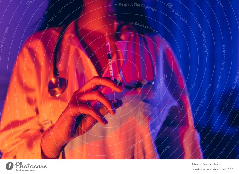 Doctor holding COVID-19, сoronavirus vaccine in the syringe using for prevent infection in ultraviolet neon light. Medicine and Healthcare concept. doctor