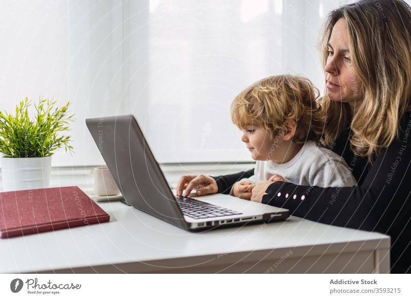 Woman with little kid working on laptop at home woman mother using together online busy remote child curious point motherhood interact parent female