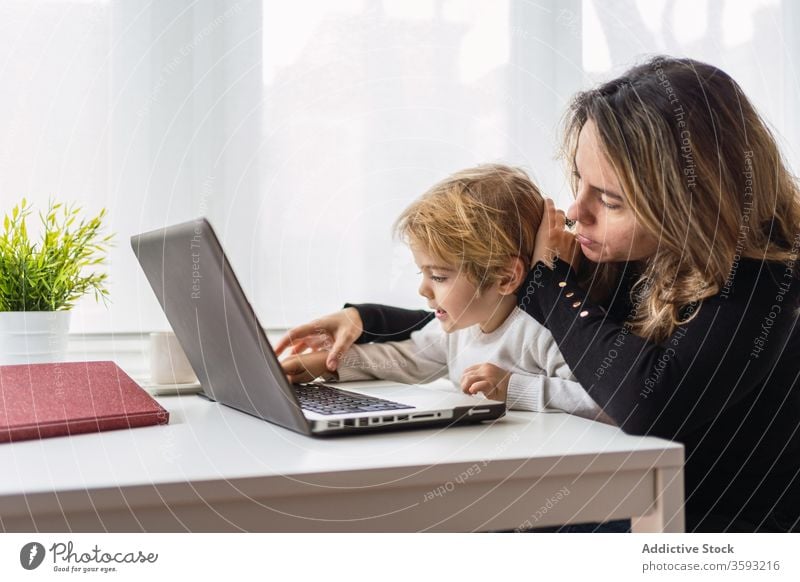 Woman with little kid working on laptop at home woman mother using together online busy remote child curious point motherhood interact parent female