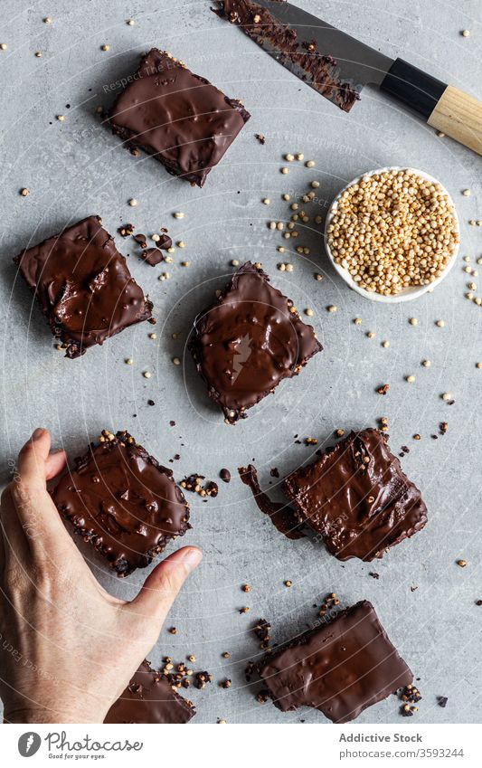 Anonymous person eating brownies covered with chocolate and quinoa seeds homemade delicious bar dessert confectionery sweet parchment knife dark cookie piece