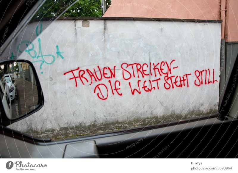 Graffiti with text photographed on a wall through a side window of a car." Women on strike- the world stands still." Equal rights, reference to the important role of women in the world and the call for equality.