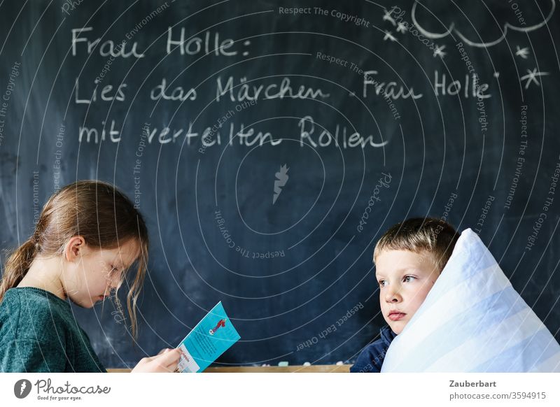 Homeschooling VI - Children read the fairy tale Frau Holle in front of a blackboard with distributed roles, the boy holds a pillow School Mother Holle