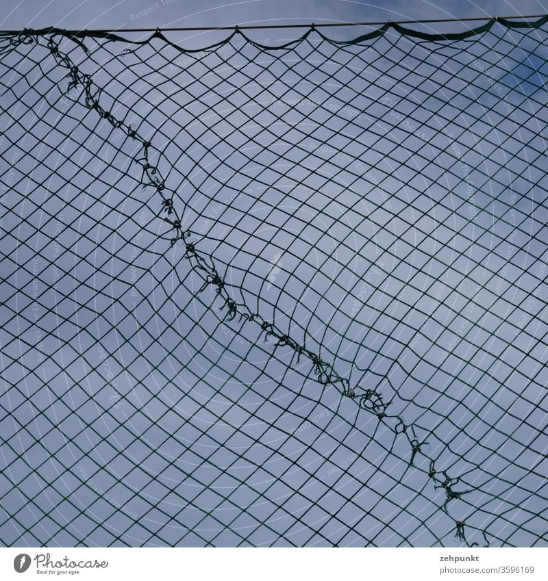 A patched fence already protects against balls flying on, which is diagonally patched against a grey-blue sky Fence Sky diamond pattern mended cloudy sky