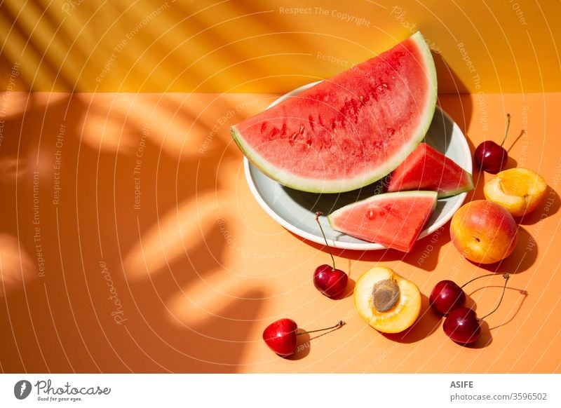 Summer fruit composition with tropical leaves shadows on orange background summer colorful watermelon still life palm cherry apricot yellow copy space monstera