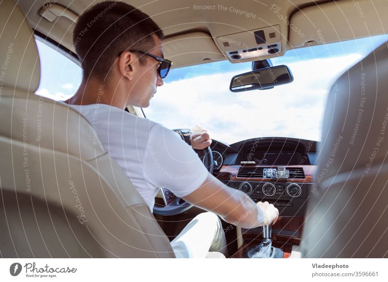 Young stylish man in sunglasses driving a car. View from the back, with the rear passenger seat. male vehicle automobile inside road day one wheel transport