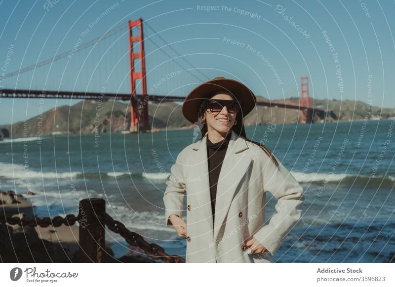 Stylish woman standing on waterfront with bridge in background trendy style travel happy smile young enjoy female tourism san francisco golden gate california