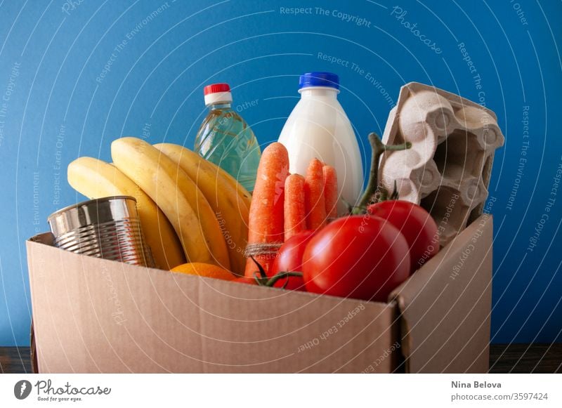 Food delivery.box with grocery. On blue background. tomatoes,bananas,milk,eggs,canned food,oil. Donation. donate service giving charity assistance social