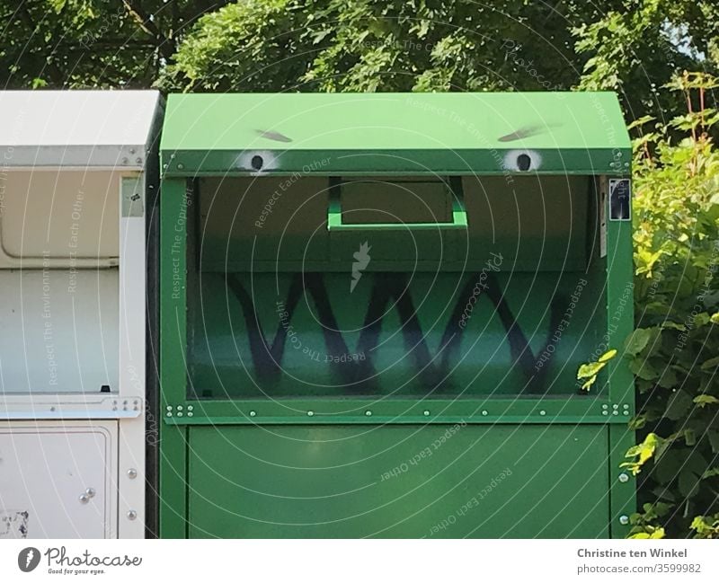 Please be friendly / Green old clothes container with painted face stands in the sunshine in front of green bushes and trees Old clothes container Container