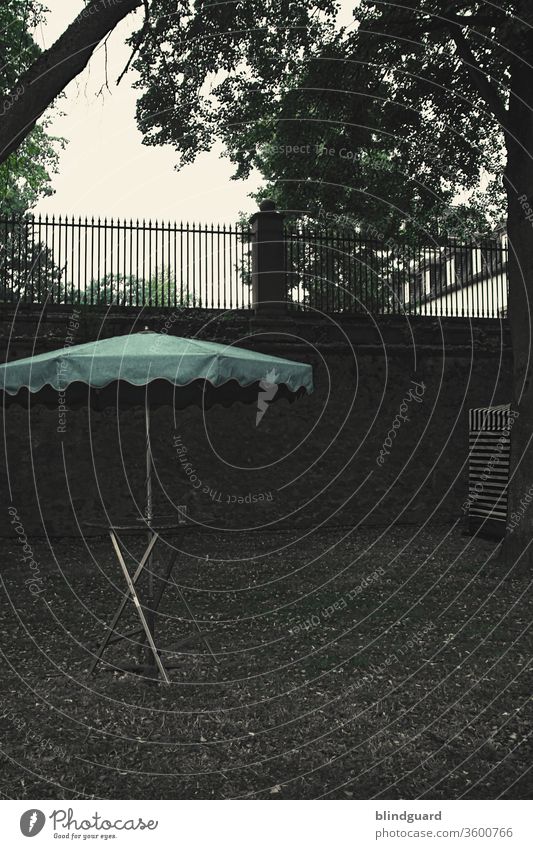 Party without people. Tristesse Deluxe. Standing table with parasol and an empty glass in front of a wall, at an event where, however, due to corona regulations and event bans, people are not allowed to participate.