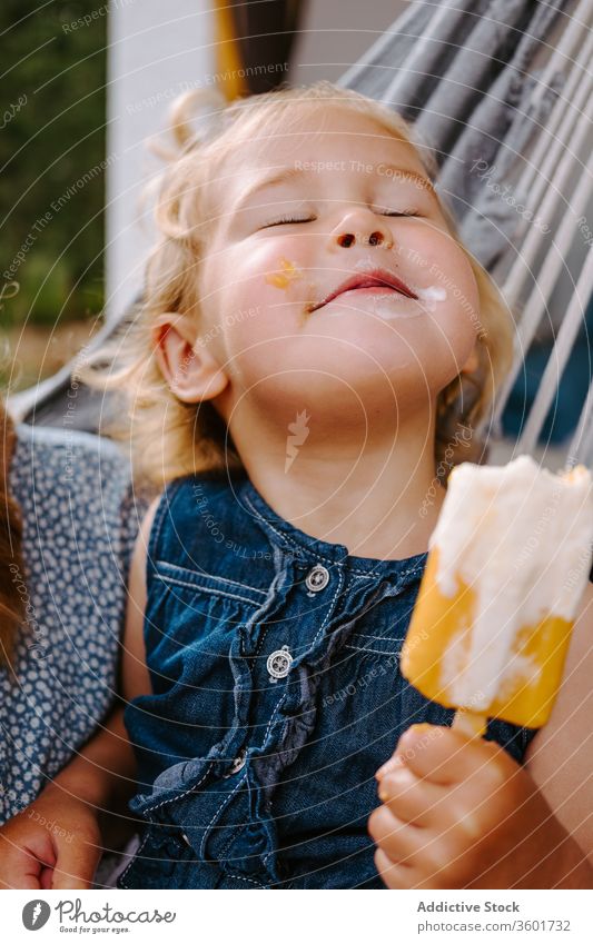 Dreamy girl with ice cream in hammock eat popsicle summer terrace homemade kid little content child childhood relax carefree enjoy adorable cheerful chill food