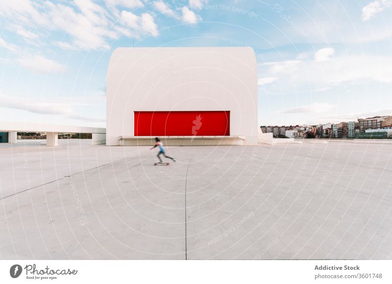 Unrecognizable skater riding board near modern building architecture design shape color creative structure square culture concrete curve construction