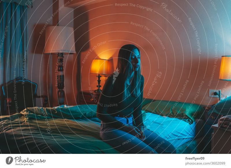 Young woman sadly sitting on the bed portrait female night quarantine depression pillow coronavirus covid-19 isolation self-isolated insomnia blue orange 30s