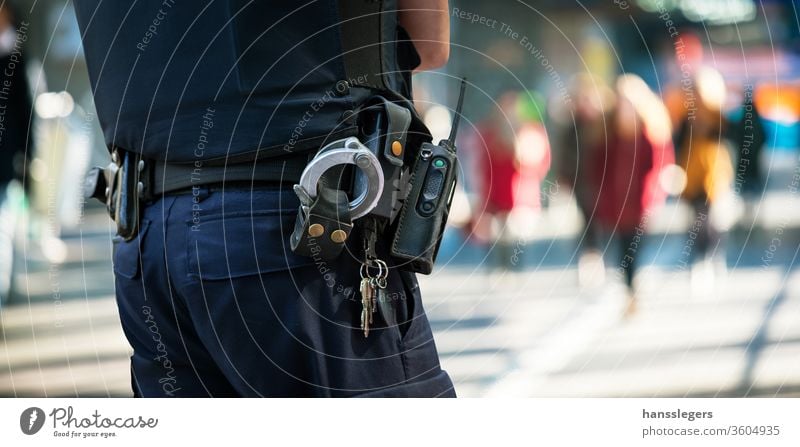 policeman with blurred people in background police officer watching handcuffs crowd street security city control cop crime criminal duty emergency enforcement