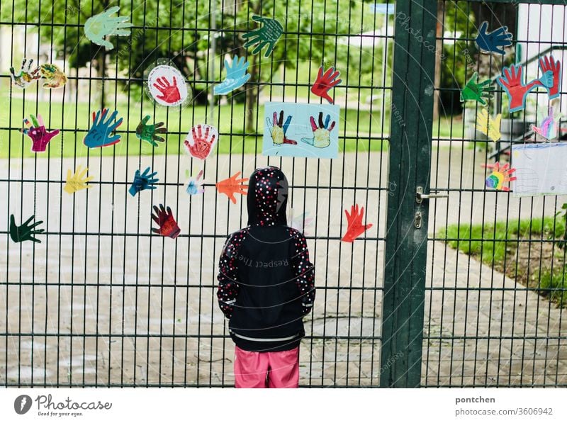 A child in rainwear stands sadly in front of a closed kindergarten.  exit restrictions, corona, closures Child Longing Kindergarten Closed hands Goal Garden