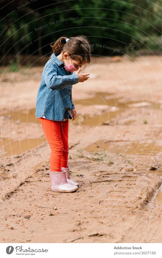 Curious girl surgical mask playing in mud puddle child having fun curious kid rubber boot cute dirty water wet adorable childhood joy activity playful ripple