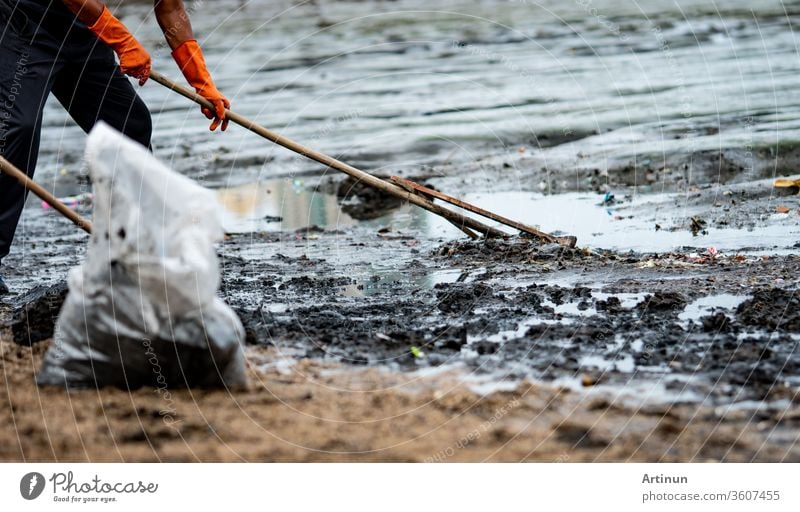 Volunteers use the rake to sweep the trash out of the sea. ฺBeach cleaner collecting garbage on the sea beach in to transparent plastic bag. Volunteers cleaning the beach. Tidying up rubbish on beach.