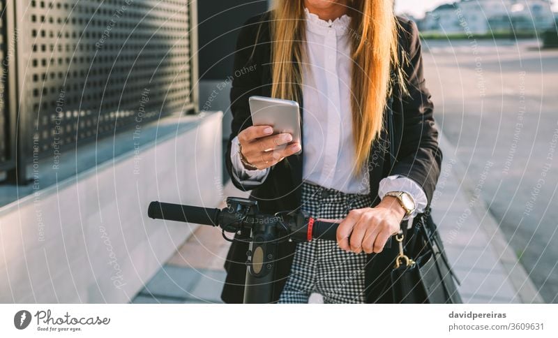 Unrecognizable businesswoman with e-scooter looking at cellphone unrecognizable city street fashion mobile worker stylish people girl young female urban person