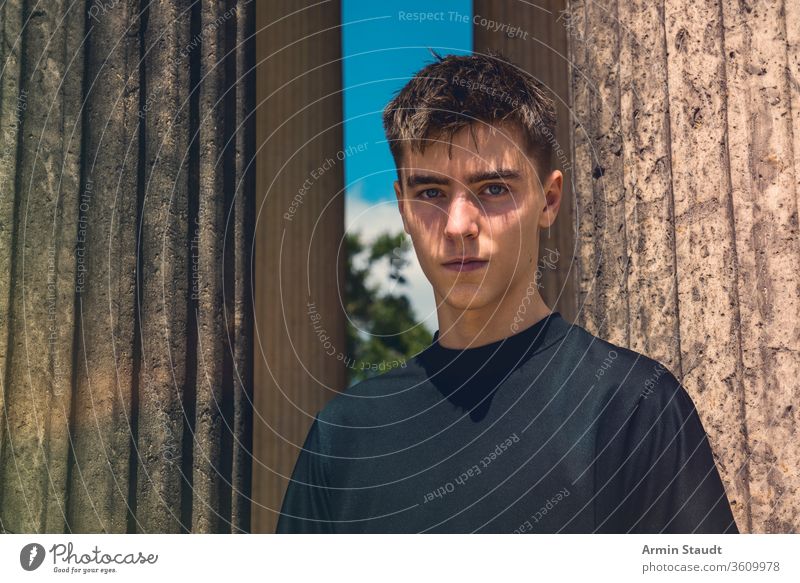 portrait of a young man standing between ancient columns teenager male outdoor pillar architecture beautiful black blue boy casual caucasian clothes