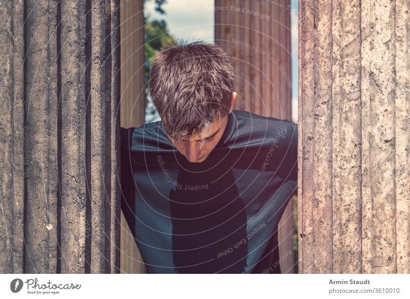 portrait of a young man standing between antique columns and looking down teenager ancient lifestyle journey pillar architecture outdoor beautiful black blue