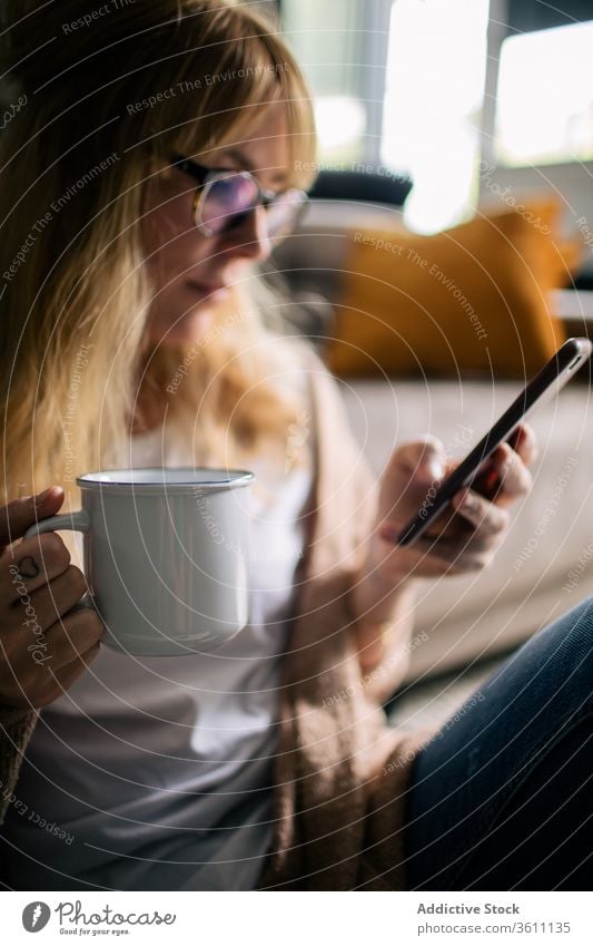 Smiling woman taking selfie on smartphone in living room relax entertain home content photo using smile female soft carpet floor sit cozy cheerful design drink