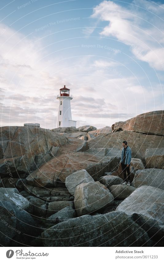 Unrecognizable male traveler admiring lighthouse in sunset man admire evening sky cloudy peggys cove canada path sundown dusk twilight nature freedom overcast