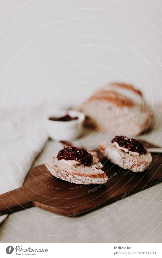 Two slice of home made organic sourdough bread slice with butter and raspberry jam on a wooden chopping board with spoon and loaf of bread and napkin. Healthy breakfast idea for vegetarians