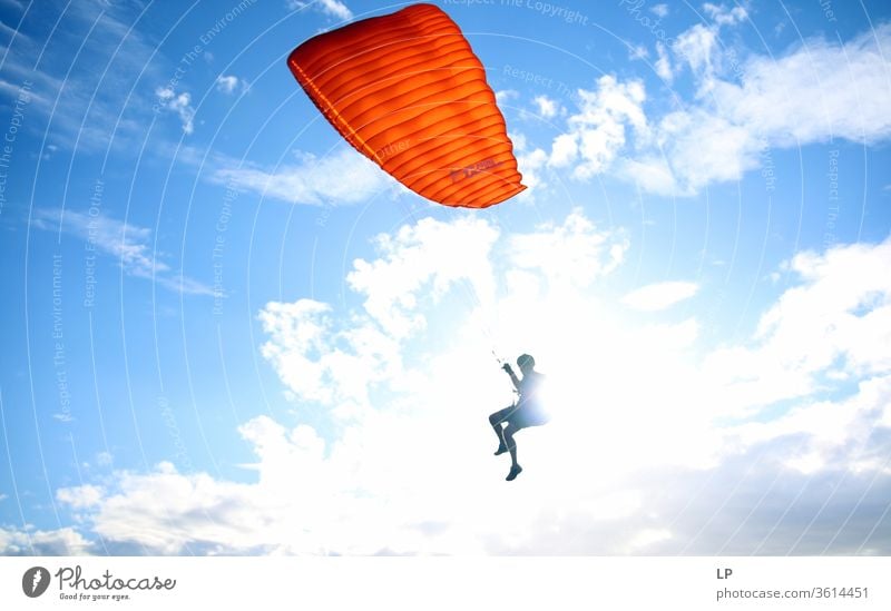 paragliding man with orange paraglider against the sun Paragliding Sunlight Sky Sports Beginning Joy Sky blue Flying Blue Warmth Contrast Paraglider Freedom