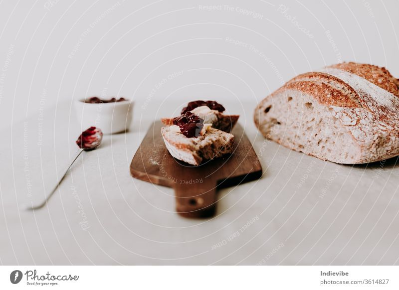 Two slice of home made organic sourdough bread slice with butter and raspberry jam on a wooden chopping board with spoon and loaf of bread and napkin fresh