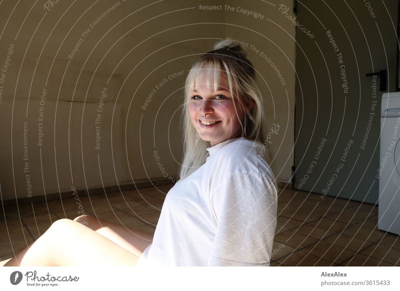 Portrait of a young blonde woman in a room with tiles girl Young woman already smile Blonde long hairs blue eyes Skin youthful 19 18-20 years 15-20 years old