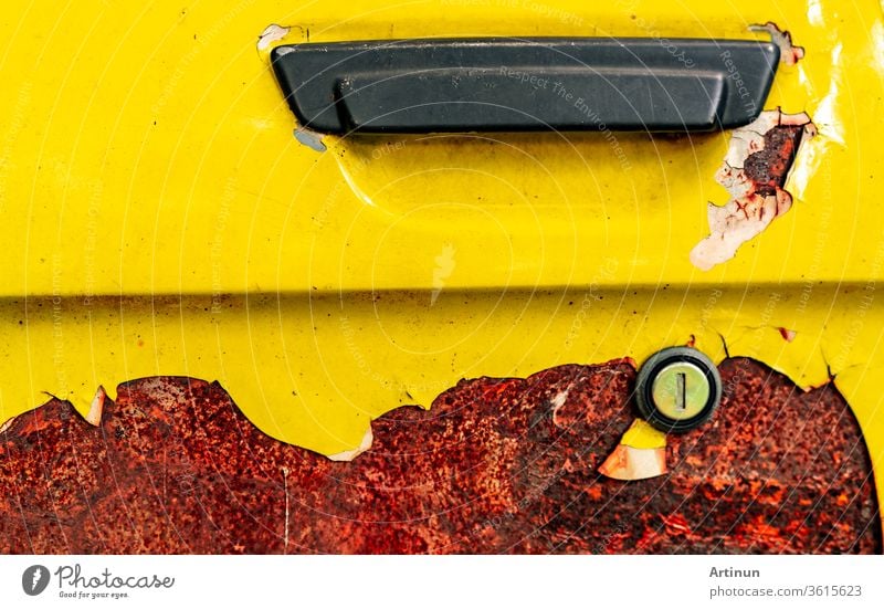 Close up old car door with rusty. Abandoned rusty yellow car with black handle. Car coloring is peeling. Old and rusted automobile door texture background. Cracked paint. Hole of auto key.