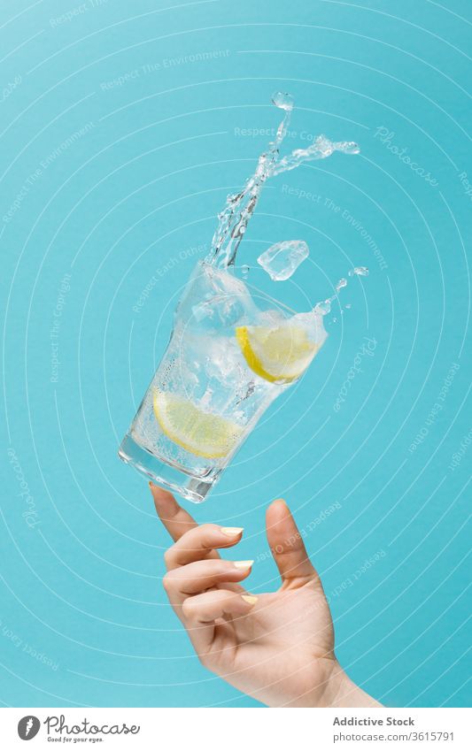 Crop woman with lemon water in studio diet concept splash refreshment toss glass female ice cold beverage fruit summer citrus cube liquid cool drink delicious