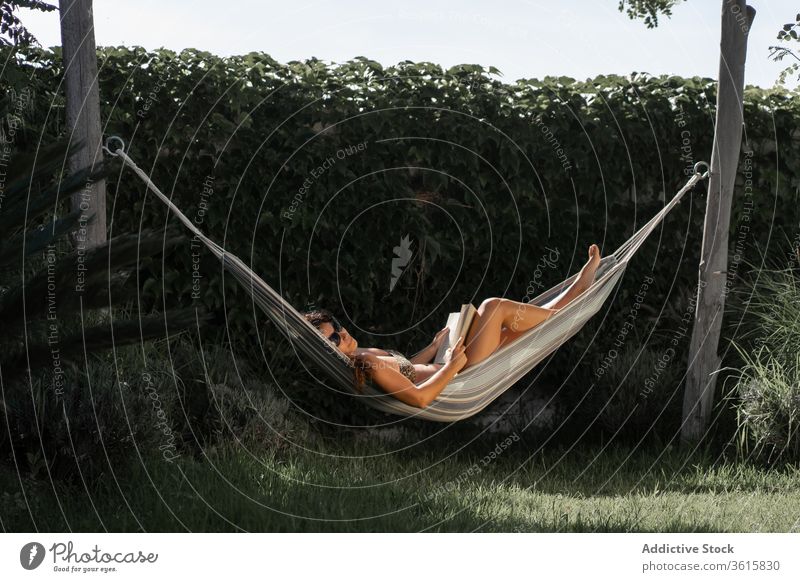 Relaxed woman with book resting in hammock relax chill summer read lying garden holiday vacation recreation lifestyle tranquil enjoy nature female young tan