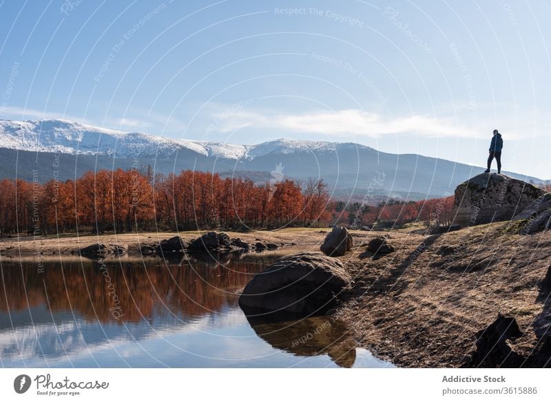 Male traveler on stone near lake in autumn landscape man mountain explorer lakeside admire male spectacular rock warm clothes outerwear season cold sunny