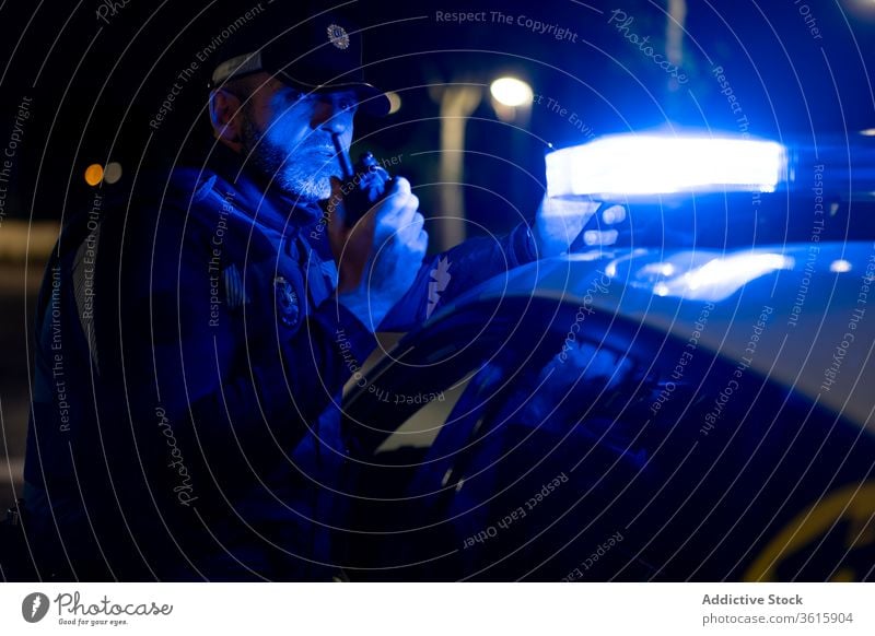 Policeman talking on walkie talkie near patrol car police officer policeman radio set siren light male automobile flash vehicle transport night speak