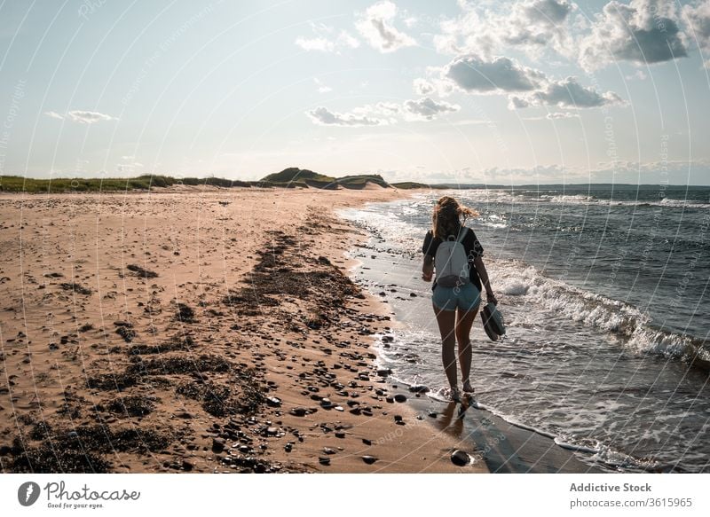 Traveling woman walking along seashore seaside vacation beach tourist summer sunny travel female barefoot journey holiday trip weekend idyllic seascape coast